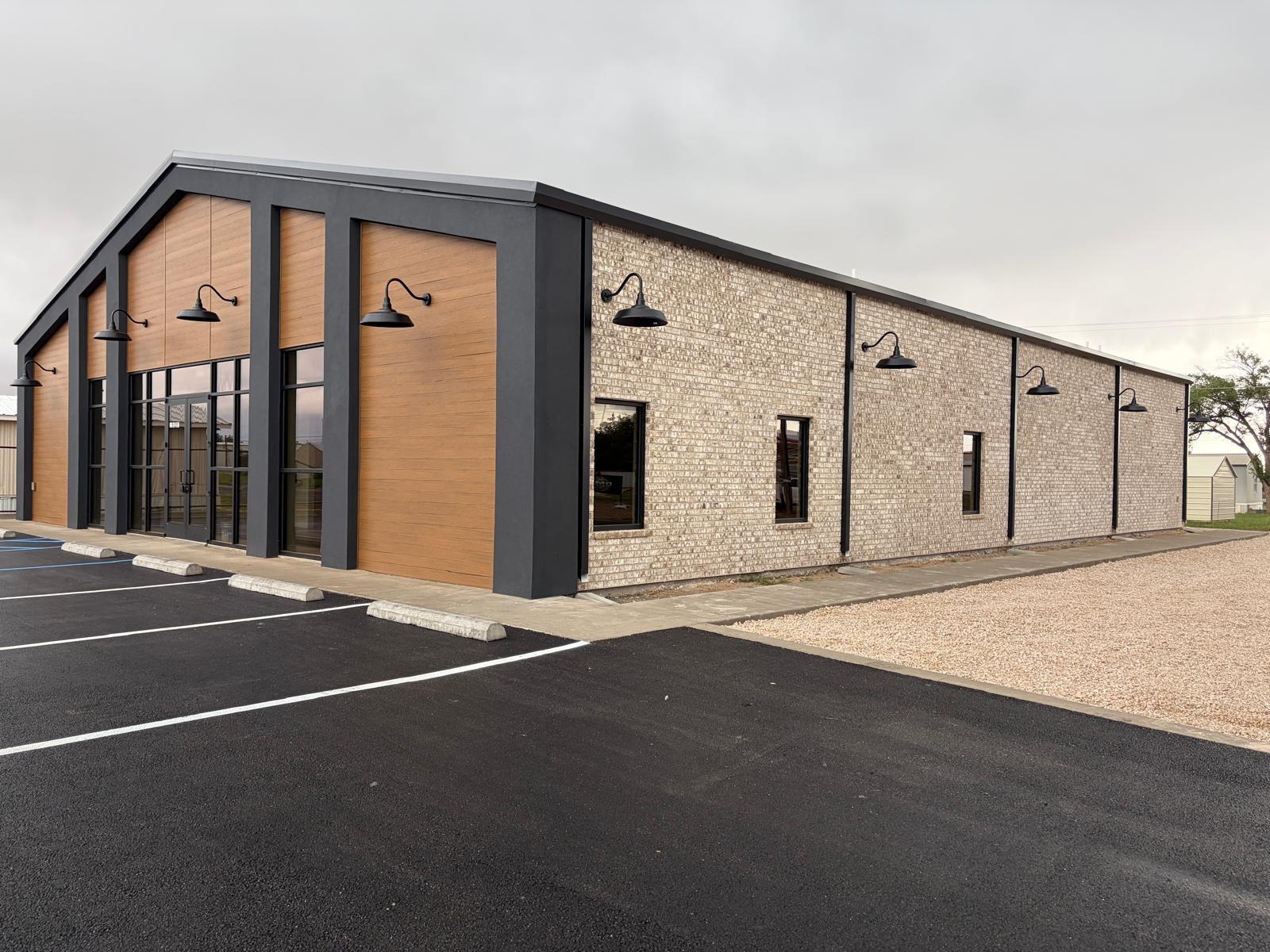 Finished metal building with charcoal steel columns, wood accent panels, and brick facade on a new asphalt lot in West Texas